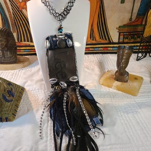 May include: A unique necklace with a black choker and a pendant featuring denim, leather, and feathers. The pendant includes the word "Lee", seashells, and silver accents. The necklace is displayed on a white mannequin.