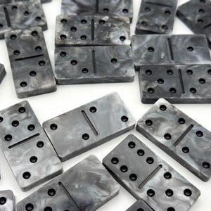 May include: A collection of grey and white marbled dominoes. Each rectangular tile has black dots indicating the numbers, and a central line divides the tile. The dominoes are arranged on a white surface.