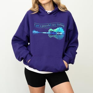 May include: Purple hoodie with a graphic of a guitar and trees with the text "I got a peaceful easy feeling" printed on the front.
