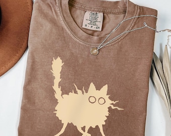 Op de afbeelding: Espresso-kleurig T-shirt met een beige kattenafbeelding. Het shirt heeft een ronde hals en korte mouwen. Een zilveren ketting met een kleine hanger is over het shirt gedrapeerd. De tekst "Espresso" staat onderaan de afbeelding.