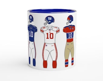 May include: White ceramic coffee mug with a blue rim. The mug features three football players wearing different New York Giants uniforms. The players are wearing jerseys with the number "10" on them. The mug is a great gift for any Giants fan.