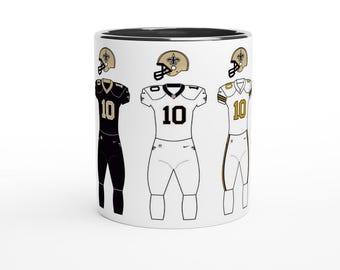 May include: A white ceramic mug with a black rim features three different football uniform designs. The uniforms are black, white, and gold with the number "10" on the front. The mug is a great gift for football fans.