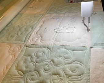 May include: A close-up of a longarm quilting machine stitching a green and white quilt. The quilt has a floral design in the center and a swirl pattern on the green fabric.