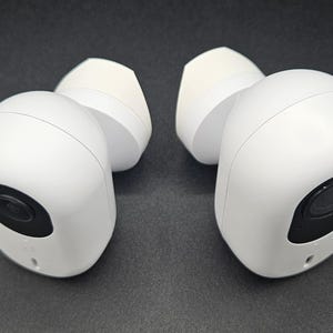 Puede incluir: Un par de auriculares inalámbricos blancos con micrófonos negros. Los auriculares tienen una forma redondeada y un acabado liso y brillante.