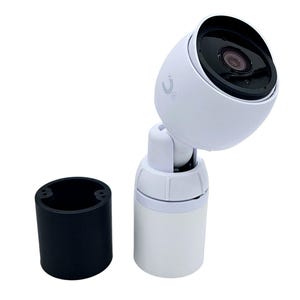 May include: A white security camera with a black lens and a white base. The camera is mounted on a white stand with a black base. The camera is angled to the right.