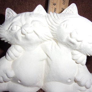 May include: A white ceramic sculpture of two cats embracing. The cats have detailed fur textures, expressive faces, and are posed in a loving embrace. The sculpture is unpainted, ready for customization.