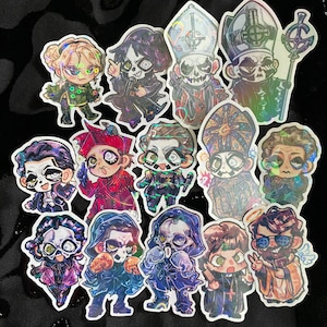 May include: A collection of colorful, holographic stickers featuring cartoon-style illustrations of characters in various outfits. The stickers have a glossy finish and are arranged on a black surface. The characters have skull-like faces and are in various poses.