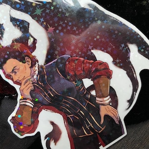 May include: A sticker of a man with dark hair and a red and black outfit, with a large black and red wing behind him. The sticker has a holographic finish with a glittery effect.