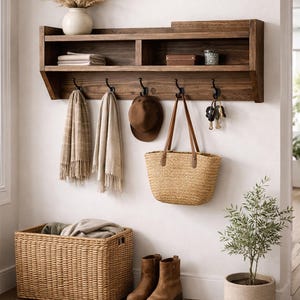 Puede incluir: Una estantería de entrada de madera con ganchos, que sostiene un sombrero, un bolso y llaves. Debajo, una cesta de mimbre y botas están en el suelo. Un jarrón con flores secas y una planta en maceta completan la decoración. La estantería mide 122 cm de ancho.