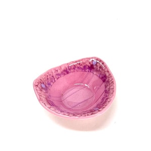 May include: A small, pink, glass bowl with a textured rim and a swirl pattern inside. The bowl is perfect for serving small snacks or dips.
