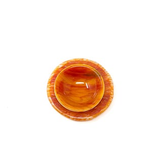 May include: A set of two decorative glass bowls in shades of orange and red. The smaller bowl sits inside a larger, matching bowl. The bowls have a marbled appearance and are set against a white background.