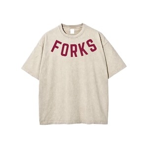 May include: Beige t-shirt with the word "FORKS" in maroon, arched across the chest. The short-sleeved shirt has a crew neck and a slightly faded appearance. The fabric appears soft and comfortable.