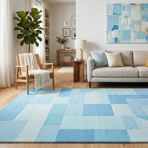May include: A modern living room featuring a large blue geometric rug. The rug's design incorporates various shades of blue. The room also includes a beige sofa with pillows, a wooden chair, and a painting with blue and white abstract shapes.