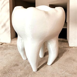 May include: A large, white, tooth-shaped sculpture with a glossy finish. The molar has three root-like legs and a wide, open top. The sculpture is set on a concrete surface.