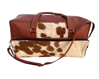 May include: A brown leather travel bag with a cowhide pattern. The bag has a long shoulder strap and two top handles.