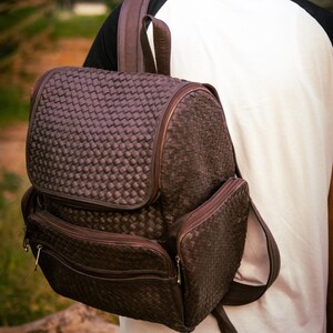 May include: A brown leather backpack with a woven pattern. The backpack has multiple pockets and a zipper closure.
