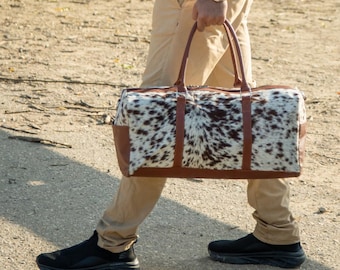 May include: A brown leather duffel bag with a white and brown cowhide pattern. The bag has two top handles and a zipper closure.