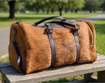 May include: A brown and black duffel bag with a textured, animal-like pattern. The bag has dark brown leather handles and straps, a side pocket, and a zipper closure. The bag is sitting on a wooden bench.