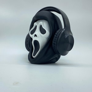 Könnte beinhalten: Eine schwarz-weiße Ghostface-Maske mit einer schwarzen Kapuze und schwarzen Kopfhörern.