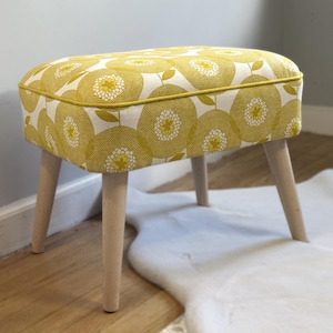 May include: A yellow and white floral patterned footstool with wooden legs.