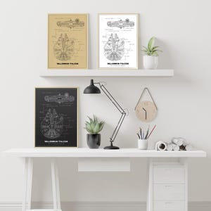 May include: Three framed prints featuring a blueprint design of the Millennium Falcon. One is on tan paper, another on white, and the third on black. Each print has the text "MILLENNIUM FALCON". The prints are displayed on a white shelf, above a desk.