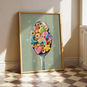 May include: A framed art print featuring a silver spoon filled with colorful cereal pieces, including hearts, stars, moons, and rainbows. The background is a muted sage green with scattered small dots and white star outlines.