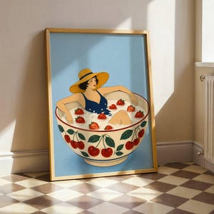 May include: A framed art print featuring a person in a dark blue swimsuit and a yellow sun hat sitting inside a large white bowl filled with milk and red strawberries. The bowl is decorated with a pattern of green leaves and red cherries.