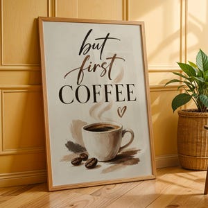 Könnte beinhalten: Ein rechteckiges gerahmtes Wandbild mit einer weißen Kaffeetasse mit Dampf, drei Kaffeebohnen und einem kleinen Herzsymbol. Der Text lautet but first COFFEE in einer Kombination aus schwarzer Schreibschrift und serifenbetonter Schrift auf Creme.