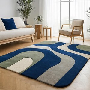 May include: A rectangular rug with a contemporary design. The rug has a flowing pattern in blue, grey, green, and cream. It's placed on a wooden floor in a living room, complementing the room's decor.