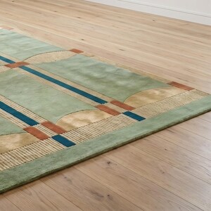Puede incluir: Una alfombra rectangular con un dise&ntilde;o geom&eacute;trico. La alfombra presenta un fondo verde claro con bordes verdes oscuros. Tiene rayas azules y &oacute;xido y formas semicirculares. La alfombra est&aacute; colocada sobre un suelo de madera clara.