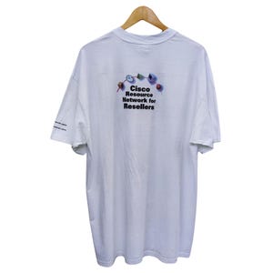 May include: White t-shirt with a graphic of a Cisco Resource Network for Resellers logo. The logo features a colorful design with a clock, computer, and other objects.