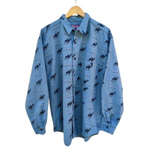 May include: A light blue button-down shirt featuring a pattern of black moose silhouettes and white wavy lines. The shirt has long sleeves and a collared neckline. The brand name "True Grit" is visible on the collar.
