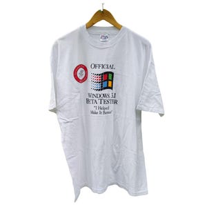 Puede incluir: Camiseta blanca con un logotipo vintage de Microsoft Windows 3.1 Beta Tester. El logotipo presenta el icónico logotipo de Windows 3.1 con el texto "OFFICIAL WINDOWS 3.1 BETA TESTER" y "I Helped Make It Better."