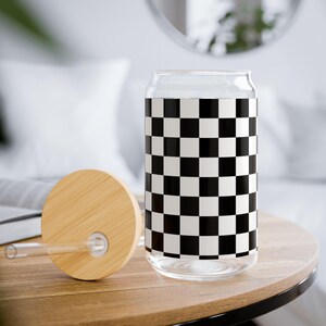 Puede incluir: Una lata de vidrio con un patrón de cuadros negros y blancos. La lata tiene una tapa de bambú con un agujero para una pajita. La pajita es de plástico transparente.