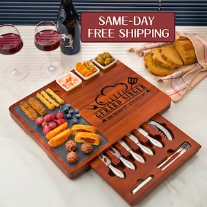 May include: A wooden serving board with a slate insert, holding various appetizers like fruit and pastries. The board has a drawer with serving utensils. A bottle of wine and two glasses are on the left. The board is engraved with "GERARD SINGER BEST COOK".