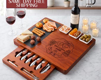May include: A rectangular wooden charcuterie board with a slide-out drawer containing metal cheese knives and forks. The board features an engraved design with two hearts, the names Robert & Sophia, and the date 12.12.2026, surrounded by food.