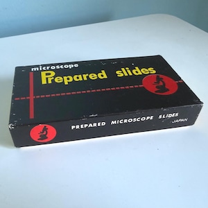 May include: A rectangular black box for microscope prepared slides. The top features yellow text reading "microscope Prepared slides" with a red graphic of a microscope. The side includes the text "PREPARED MICROSCOPE SLIDES" and "JAPAN".