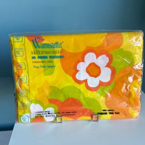 May include: A Wamsutta Ultracale standard twin flat sheet in original plastic packaging. The fabric features a vibrant yellow, orange, and lime green floral pattern. Text includes Wamsutta Ultracale, No Ironing Necessary, and Stays Fresh Longer.