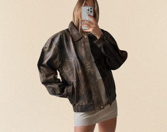 May include: A brown leather jacket with a classic collar and button closure. The jacket has a distressed, vintage look with visible wear and tear. It features two front pockets and a ribbed hem. A stylish outerwear piece.