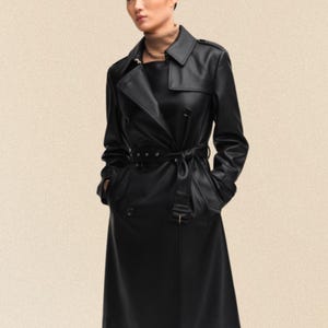 Könnte beinhalten: Ein schwarzer Trenchcoat mit doppelreihigem Design, Gürtel und Reverskragen. Der Mantel hat lange Ärmel und Taschen. Das Model trägt einen Rollkragenpullover unter dem Mantel.