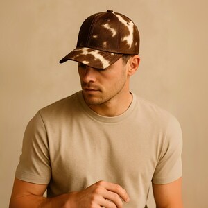 May include: A brown and white patterned baseball cap. The cap has a curved brim and a button on top. The cap is made of a textured material. The person in the image is wearing a beige t-shirt.