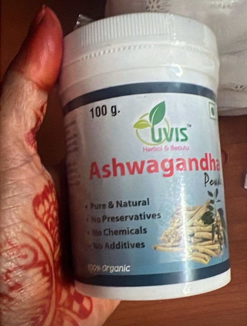 May include: A white plastic container of Ashwagandha powder, labeled "UVIS Herbal & Beauty." The container holds 100 g of powder and is marked as pure, natural, and organic, with no preservatives, chemicals, or additives.