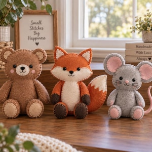 May include: Three handmade felt plush toys featuring a brown bear, an orange and white fox, and a gray mouse with pink ears. Each animal has stitched details, black bead eyes, and a seated posture, displayed together on a wooden surface.