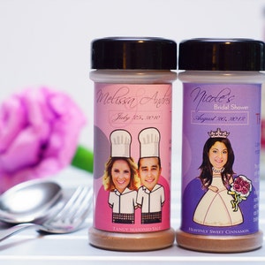 Puede incluir: Dos tarros de especias con etiquetas personalizadas. El tarro rosa tiene una imagen de una pareja con gorros de chef y el texto "Melissa & Andrew July 25, 2010" y "Sal sazonada picante". El tarro morado tiene una imagen de una mujer con una corona y el texto "Nicole's Bridal Shower August 20, 2018" y "Canela dulce celestial".