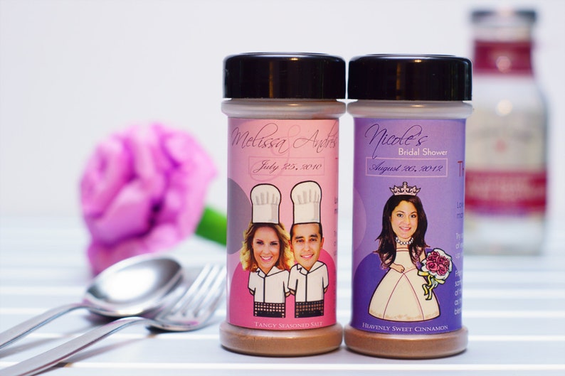 Puede incluir: Dos tarros de especias con etiquetas personalizadas. El tarro rosa tiene una imagen de una pareja con gorros de chef y el texto "Melissa & Andrew July 25, 2010" y "Sal sazonada picante". El tarro morado tiene una imagen de una mujer con una corona y el texto "Nicole's Bridal Shower August 20, 2018" y "Canela dulce celestial".