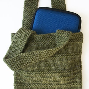 Op de afbeelding: Een groene gebreide tote bag met een blauwe ritszak aan de binnenkant. De tas heeft een lange band en is gemaakt van een dik, getextureerd garen.