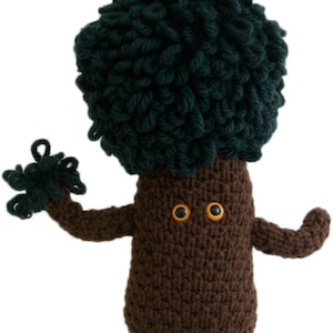 Può includere: Un giocattolo di peluche fatto a mano a forma di albero. L'albero ha un tronco e braccia marroni, una testa verde scuro e strutturata e due occhi con centri gialli. Le braccia sono tese, dando all'albero un aspetto amichevole.