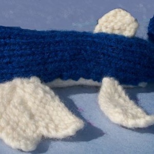 May include: A blue knitted whale with white knitted fins. The whale has a red button eye.