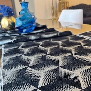May include: A black and white geometric patterned table runner with a 3D cube design. A blue glass decorative bottle with a clear stopper sits on the table. A gold vase with blue flowers is also on the table.