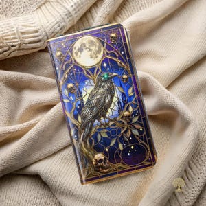 May include: A rectangular wallet featuring a stained glass style illustration of a black raven perched on a branch. The design includes a full moon, multiple skulls, and intricate web-like patterns in shades of deep blue, purple, and gold.